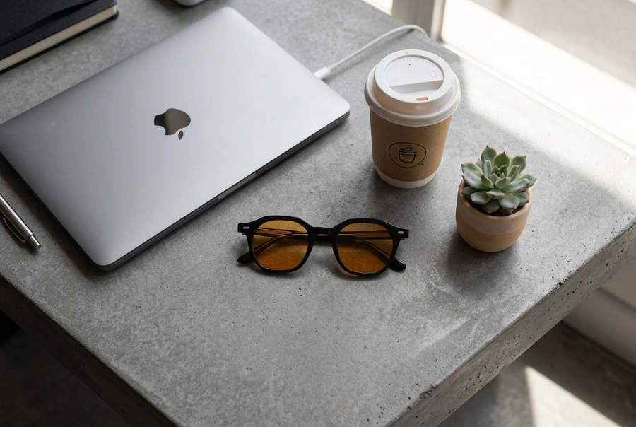 Lunettes à verres orange posées sur un bureau à côté d'un ordinateur portable, d'un café et d'une plante