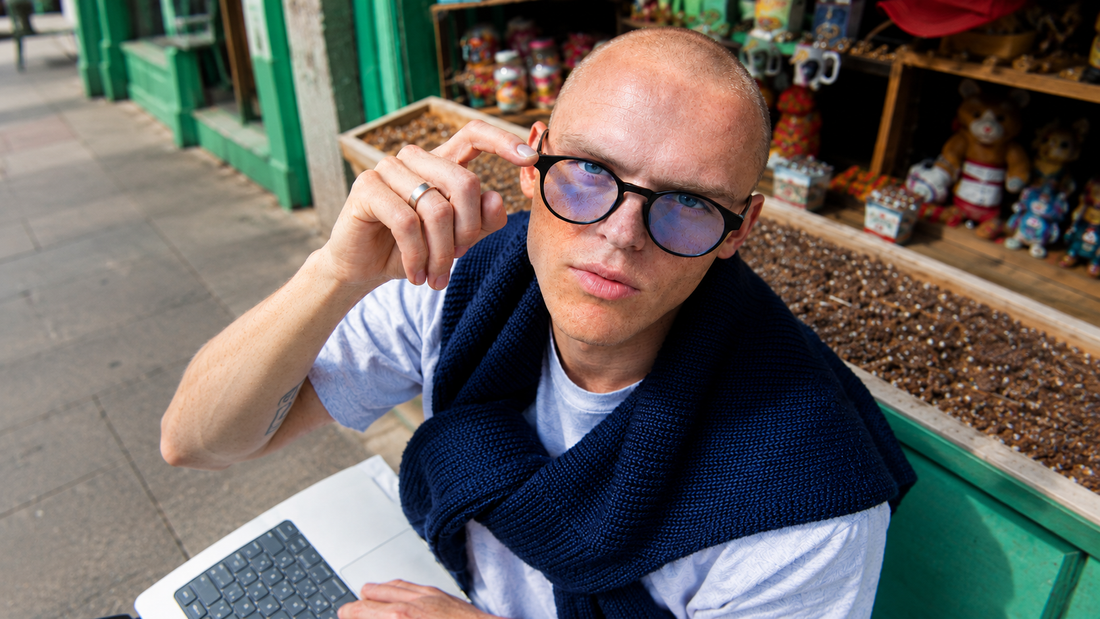 Jeune homme ajustant ses lunettes SAY rondes noires, ordinateur portable devant une vitrine