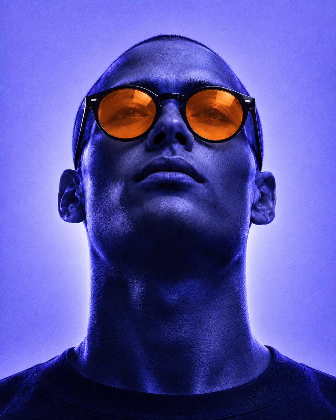 Homme portant des lunettes à verres orange sous une lumière bleue, le regard levé