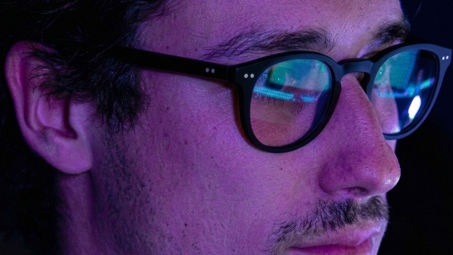 Développeur portant des lunettes rondes noires, reflets d'écran bleus sur les verres