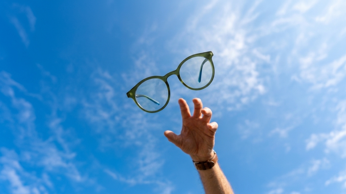Main tendue vers une paire de lunettes rondes vertes, dans un ciel bleu